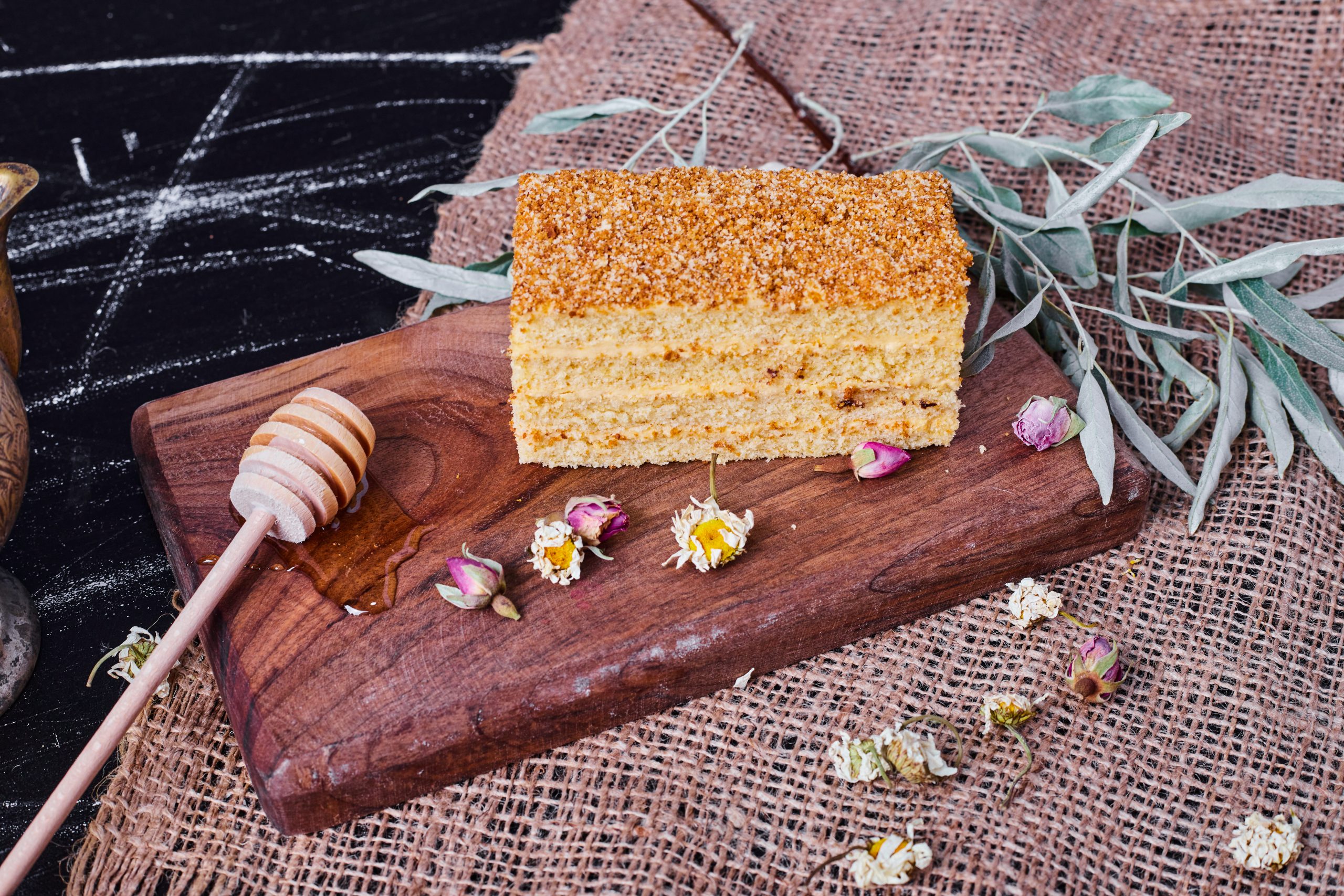 A piece of homemade honey cake with dried flowers and honey spoon on wool tablecloth A piece of homemade honey cake with dried flowers and honey spoon on wool tablecloth. High quality photo